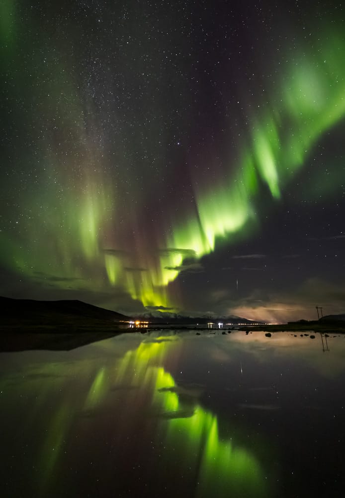 Vibrant green Northern Lights illuminating a starry night sky, reflected perfectly in calm water during a guided photography trip
