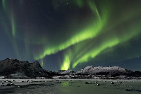 Northern Lights shimmering in the sky on a moonlit night, casting a soft glow over snow-covered mountain peaks.