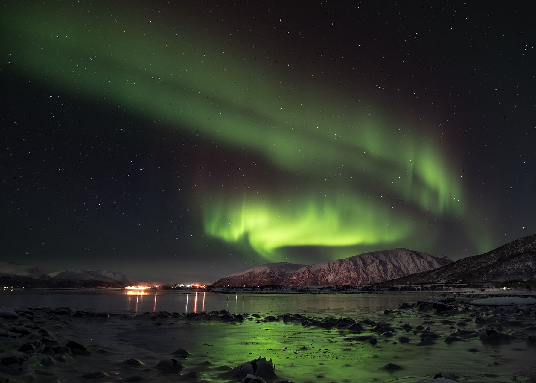 Northern Lights glowing high above icy Arctic waters, with vibrant reflections dancing across the frozen surface under a clear night sky.