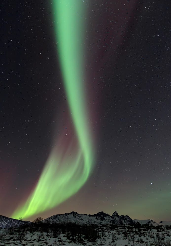 Dancing green and purple Northern Lights over snowy mountain peaks under a star-filled sky during a photography expedition