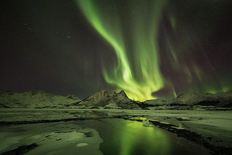 Aurora dancing across the night sky, with vibrant colours reflected in the still, mirror-like waters below.