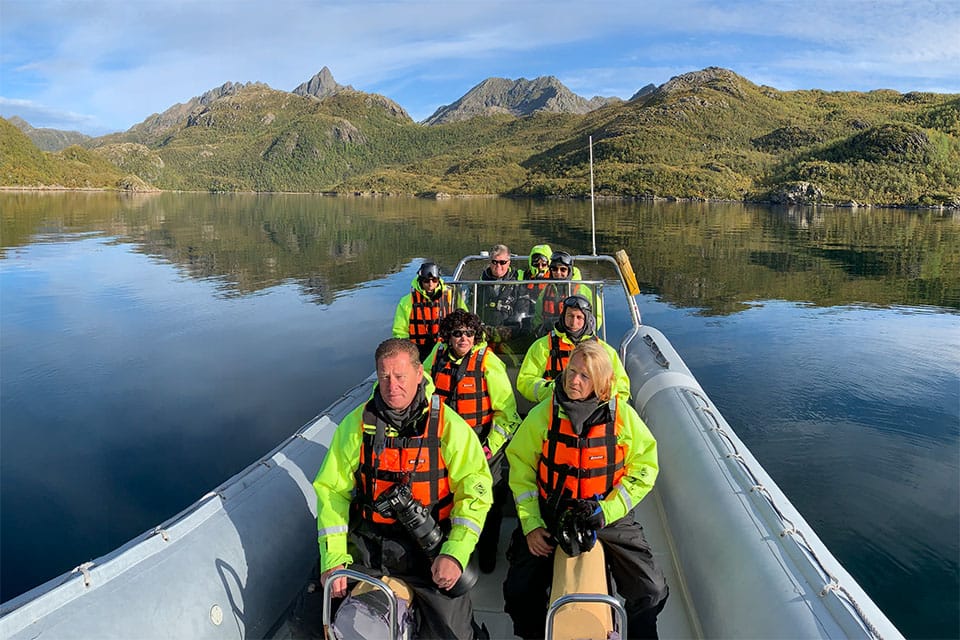 Photography guests aboard a small RIB cruising Hellfjord on a sunny autumn day, searching for sea eagles among golden-hued cliffs and calm waters.