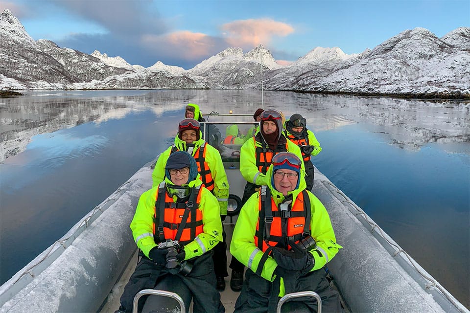 Photography guests aboard a small RIB exploring Hellfjord in winter, scanning the icy cliffs for sea eagles amid snowy Arctic landscapes.