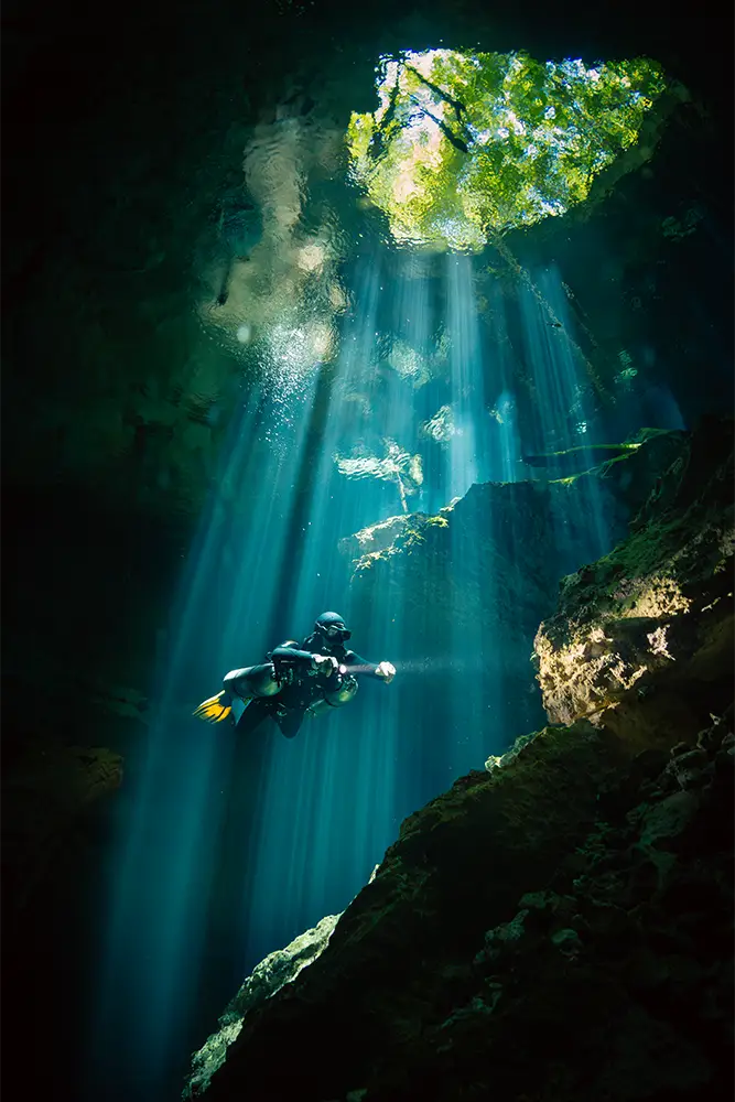 A lone diver descents into a sink hole in Mexico whilst bathed in light beams