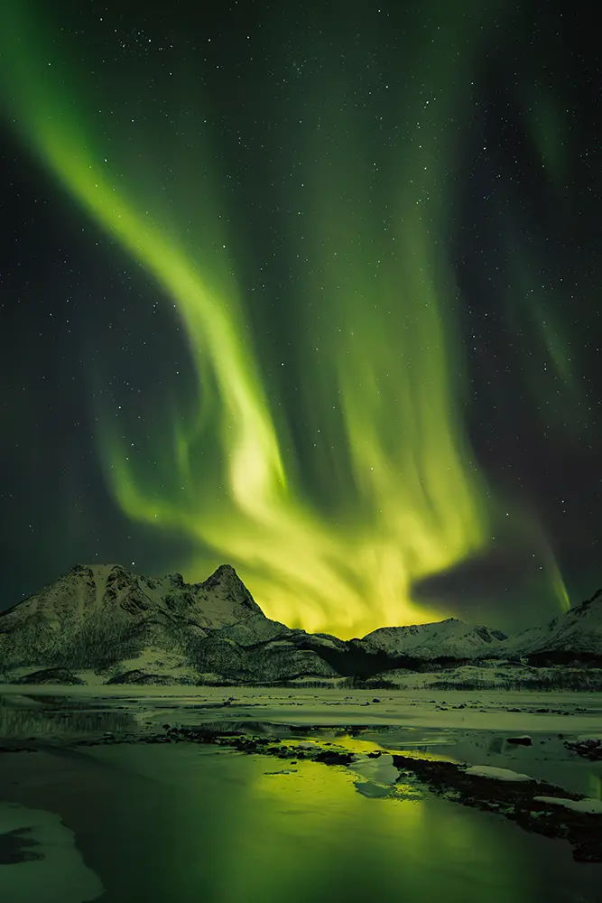 Northern lights brightly illuminate the Arctic sky over the mountains in Vesterålen during a guided photo trip
